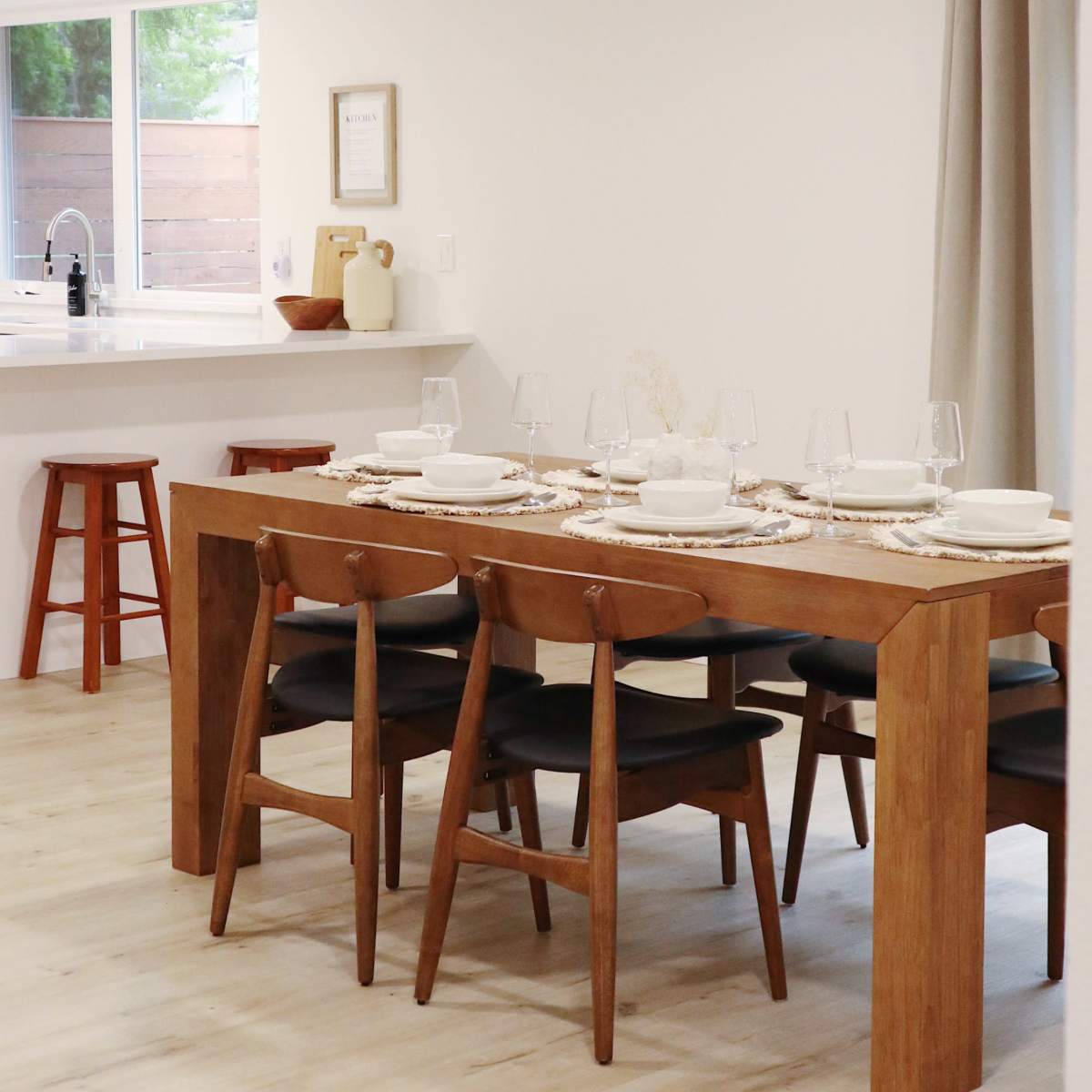 A modern dining area features a wooden table set for a meal with chairs and a window displaying a view of the outdoors.