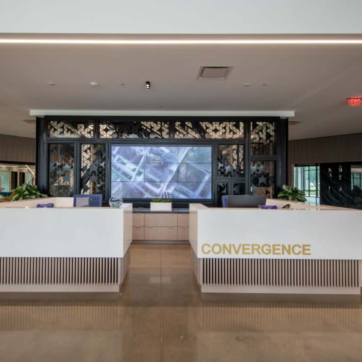 A modern reception area with two white desks labeled "CONVERGENCE" and a large screen displaying visuals in the background.