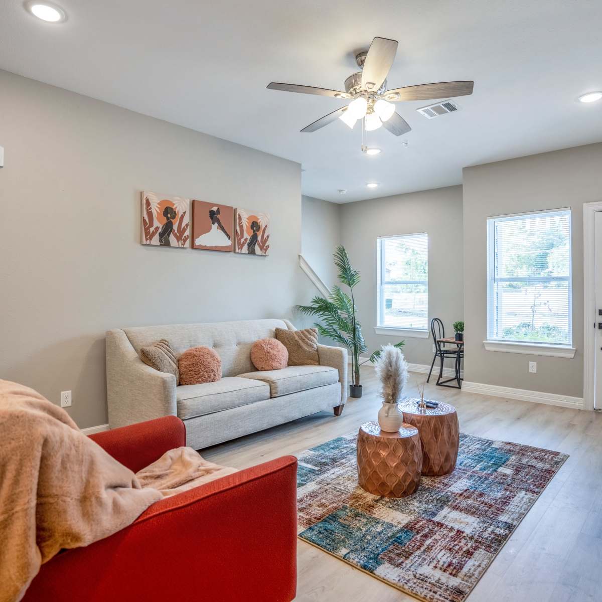 A modern living room features a light gray sofa, a red armchair, a decorative rug, and large windows that provide natural light.