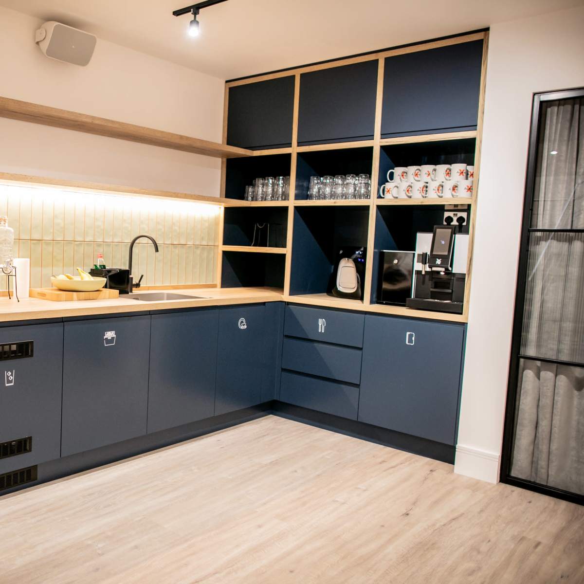 A modern kitchen with blue cabinetry, a wooden countertop, and glassware displayed on shelves.