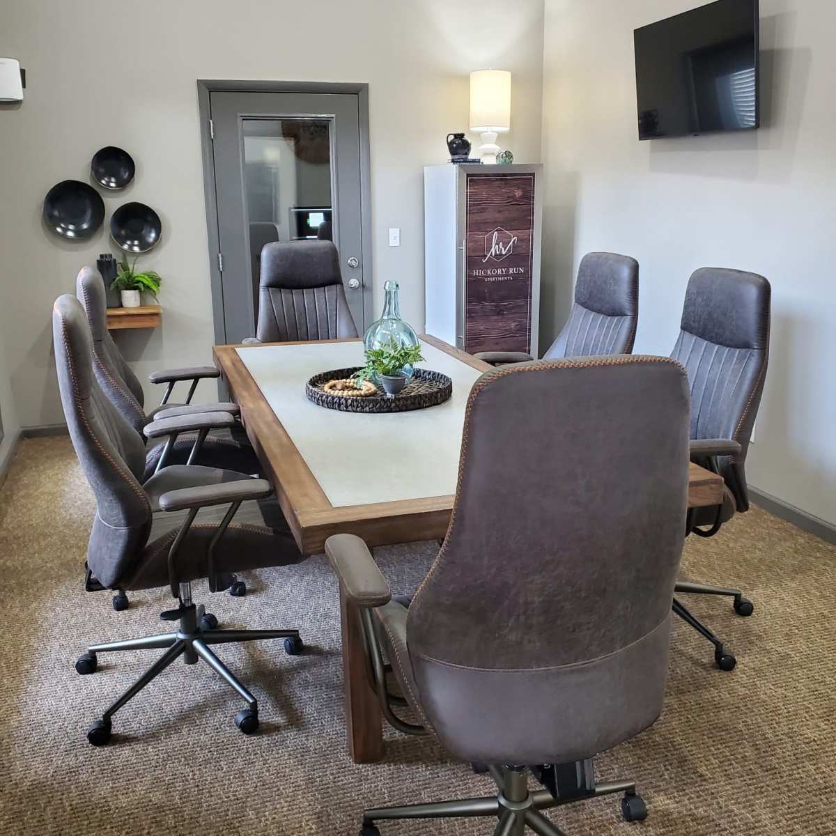 A modern conference room with a wooden table surrounded by six ergonomic chairs, a wall-mounted TV, and decorative elements.