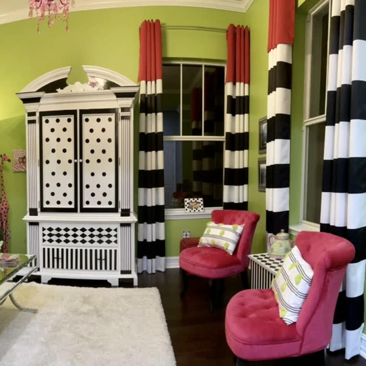 The room features a green wall, a black sofa with decorative pillows, a silver coffee table, striped black and white curtains, and a furniture piece with polka dots.