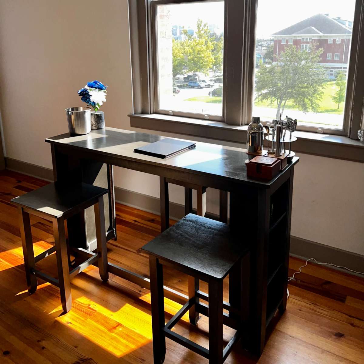 A black table with two stools is positioned near a window, featuring a vase with blue flowers and a notepad on its surface.