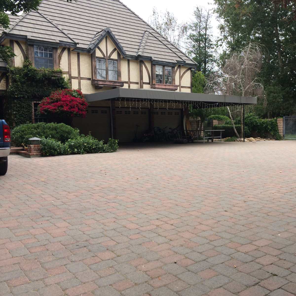 A large brick-paved driveway leads to a house with a covered entryway adorned with greenery and flowers.