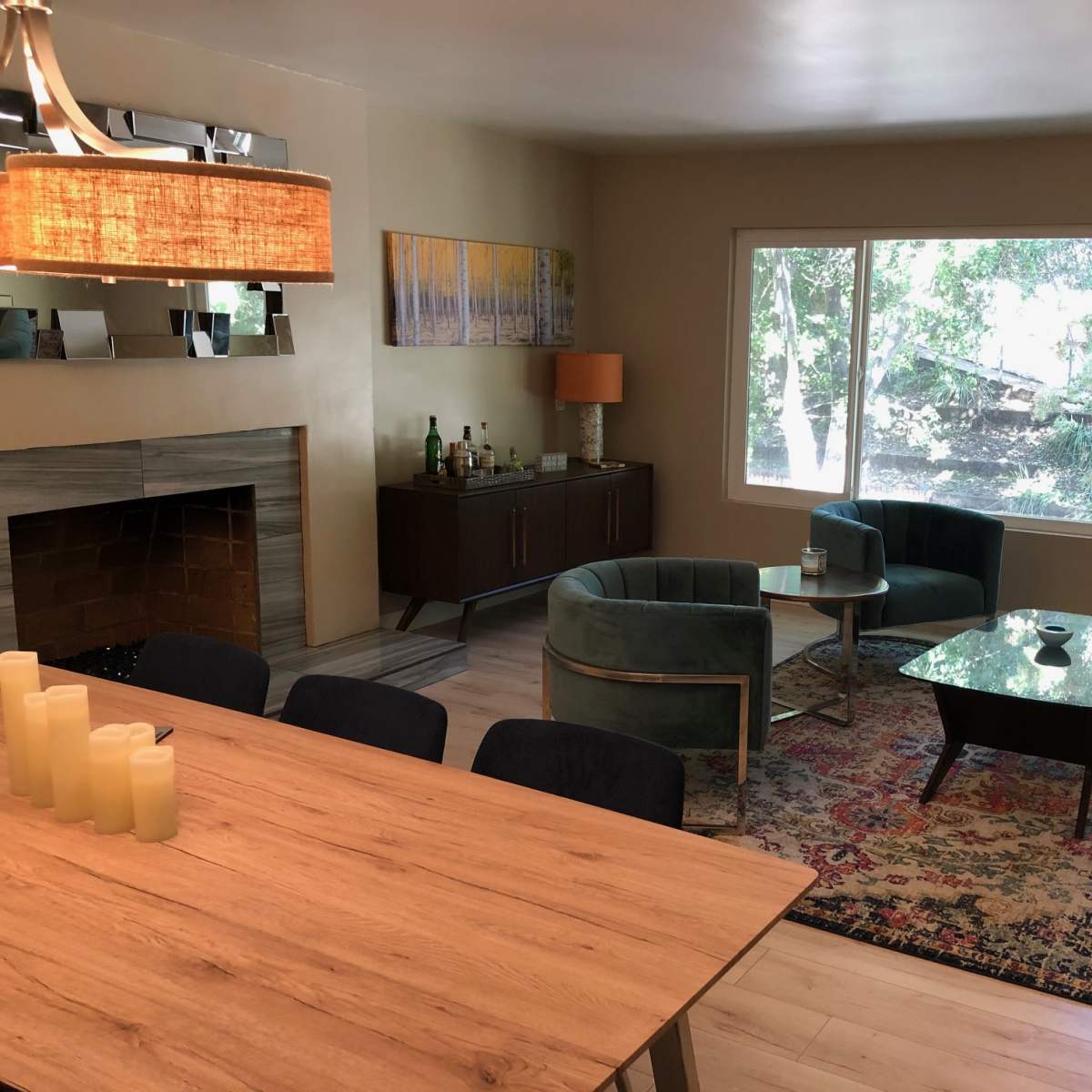 The room features a living area with a fireplace, two green chairs, a brown sofa, a coffee table, and a dining table, all arranged near large windows that provide natural light.