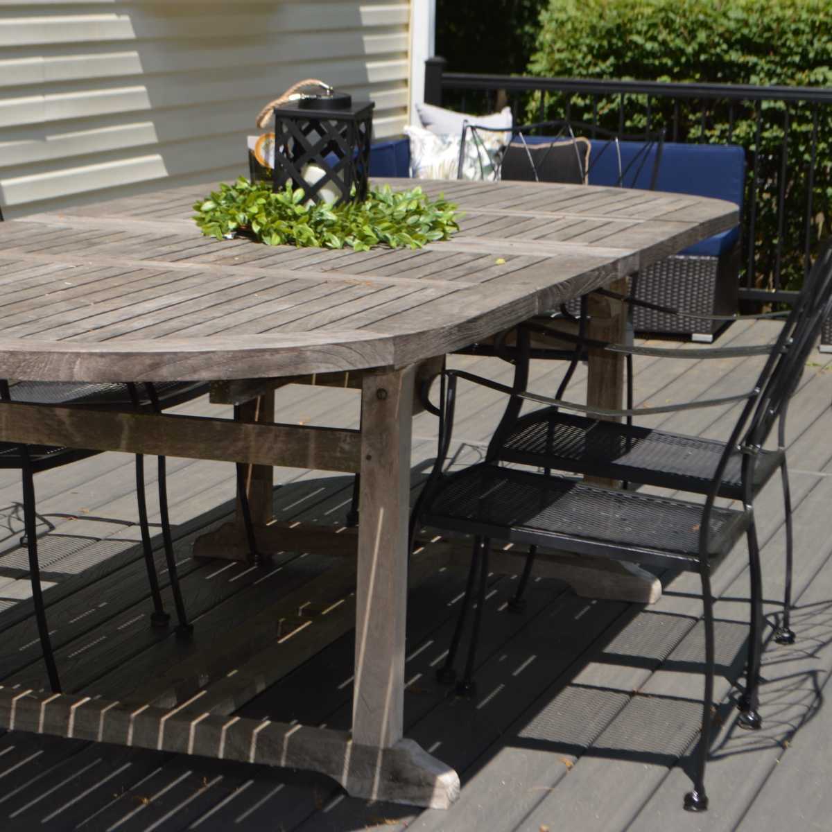 A wooden oval table with a planter sits on a deck surrounded by black metal chairs.