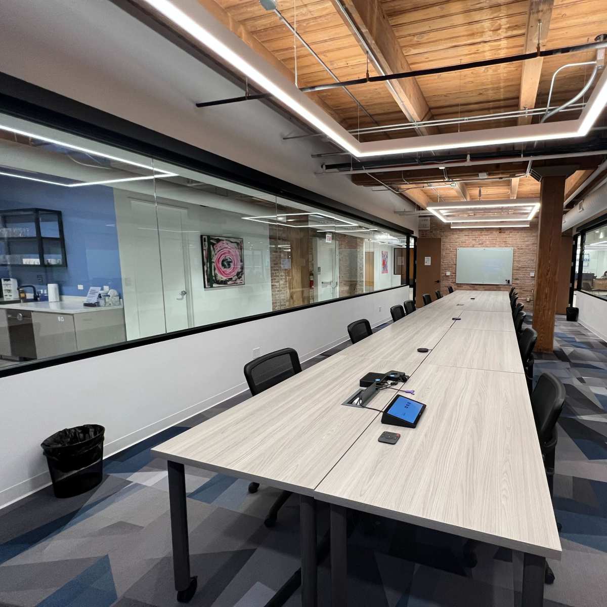 A modern conference room with a long table, black chairs, large windows, and exposed wooden beams.