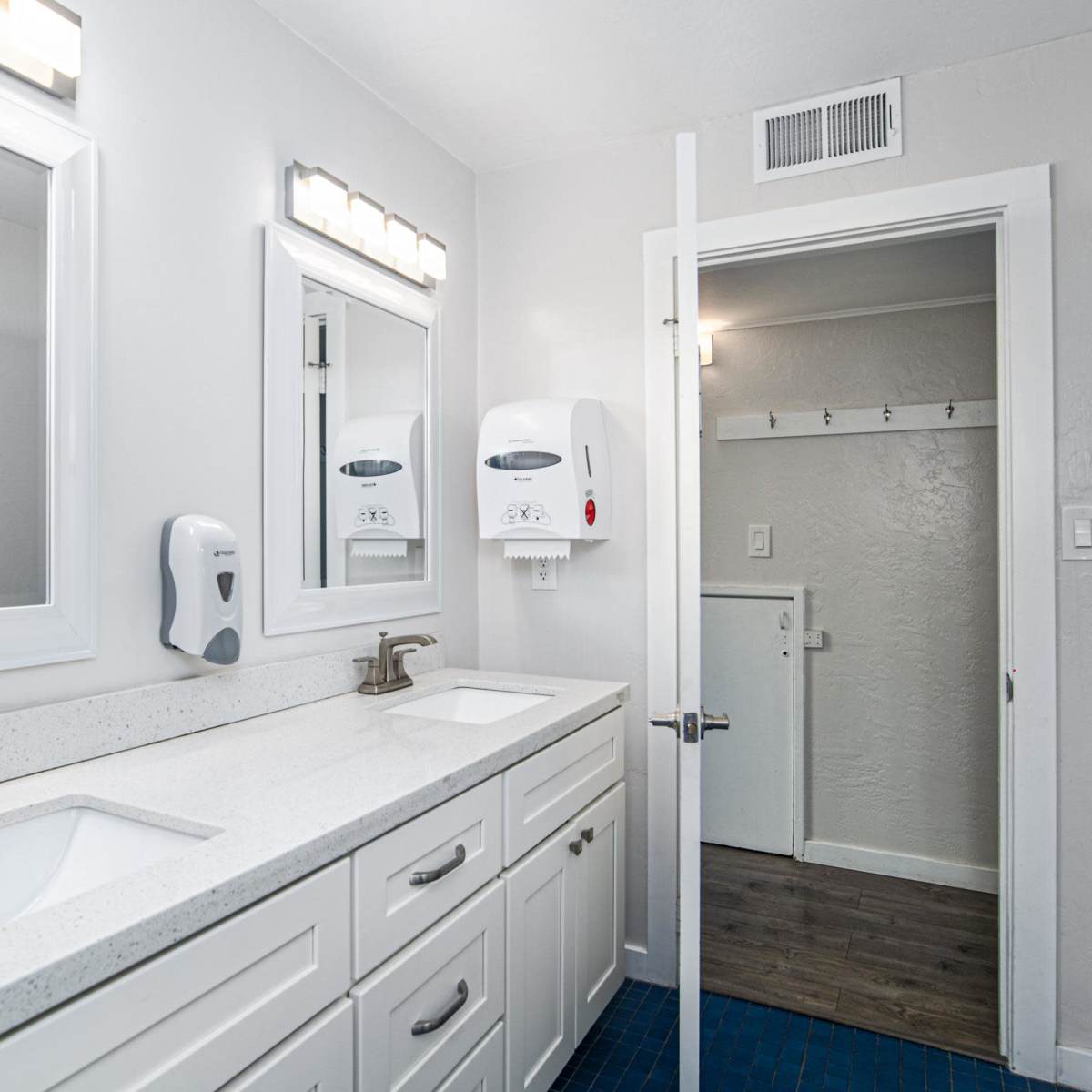 A modern bathroom with double sinks, large mirrors, and a door leading to another room.