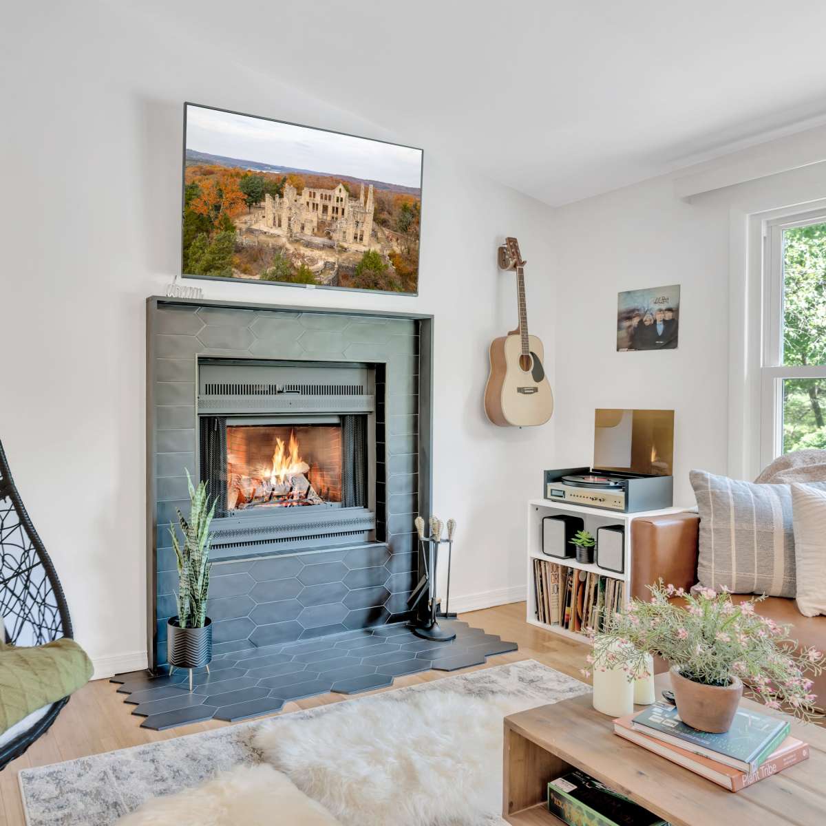 The living room features a hanging chair next to a fireplace with a television mounted above it, accompanied by a guitar, record player, and plants.