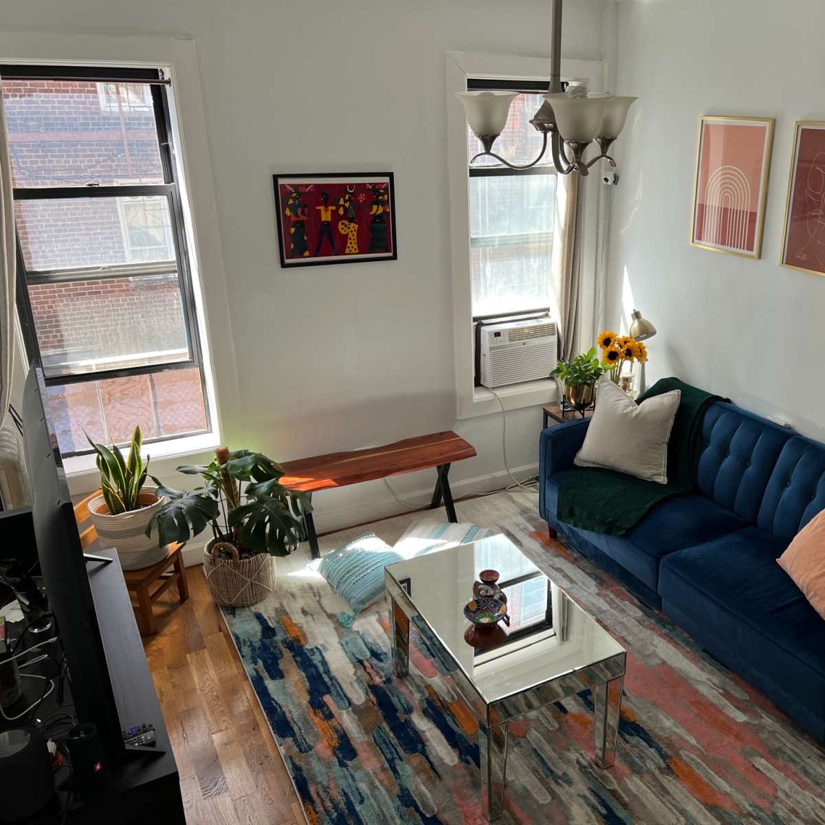 A bright living room featuring a blue couch, a wooden bench, indoor plants, and artwork on the walls.