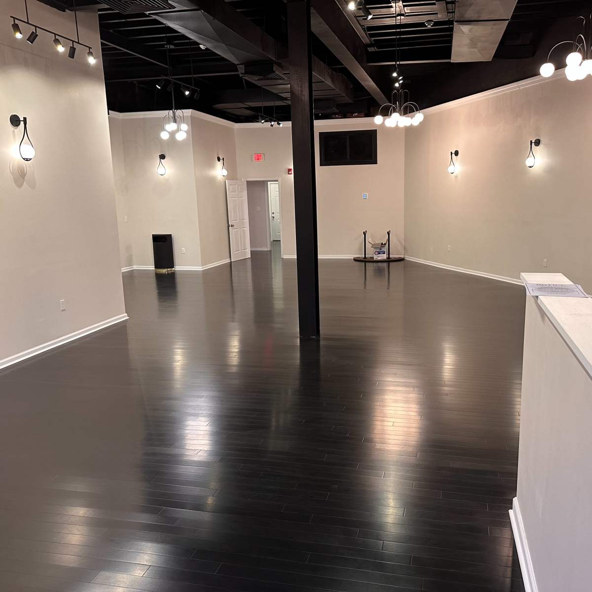 A spacious, empty room with black wooden flooring and several light fixtures mounted on the walls.