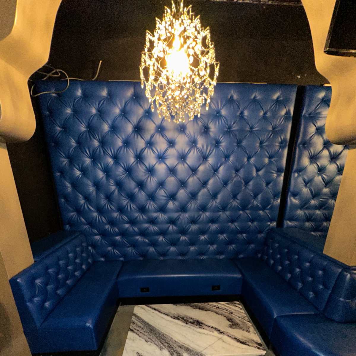 A corner seating area in a lounge, featuring blue tufted upholstery, a black marble table, and a chandelier overhead.