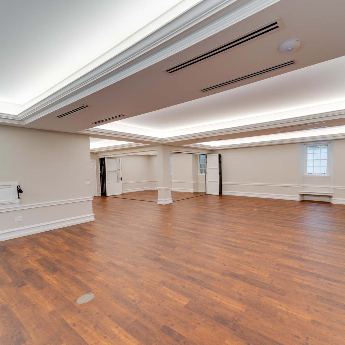 An empty room with hardwood flooring, recessed ceiling lighting, and large windows along one wall.