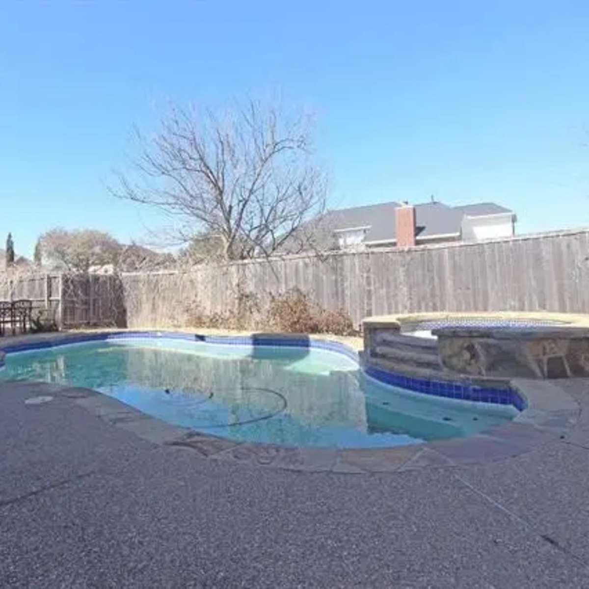 A backyard with a swimming pool, a circular hot tub, and a wooden fence surrounding the area.