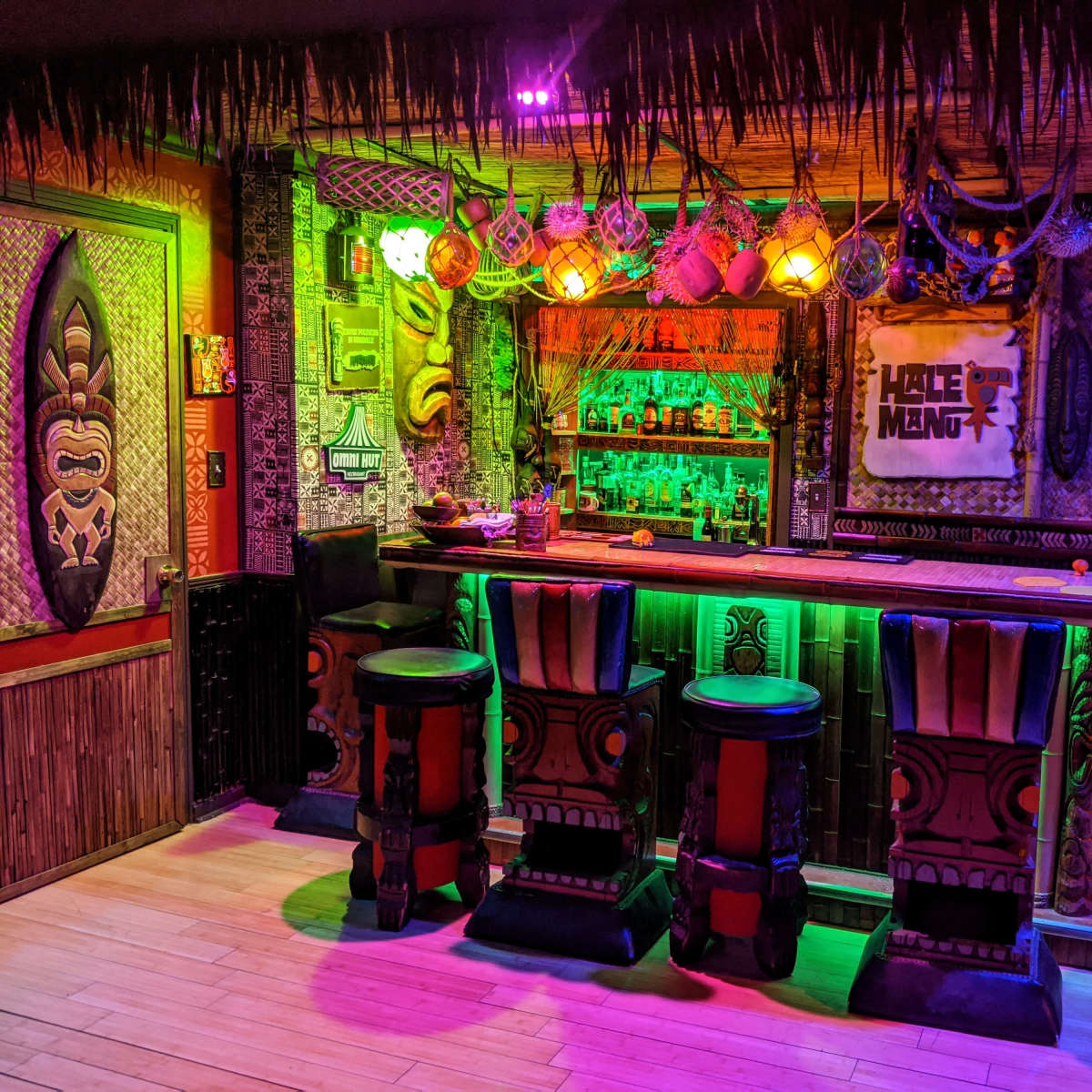 A vibrant tiki bar featuring colorful lighting, a wooden bar with decorative stools, and tropical-themed decor on the walls.