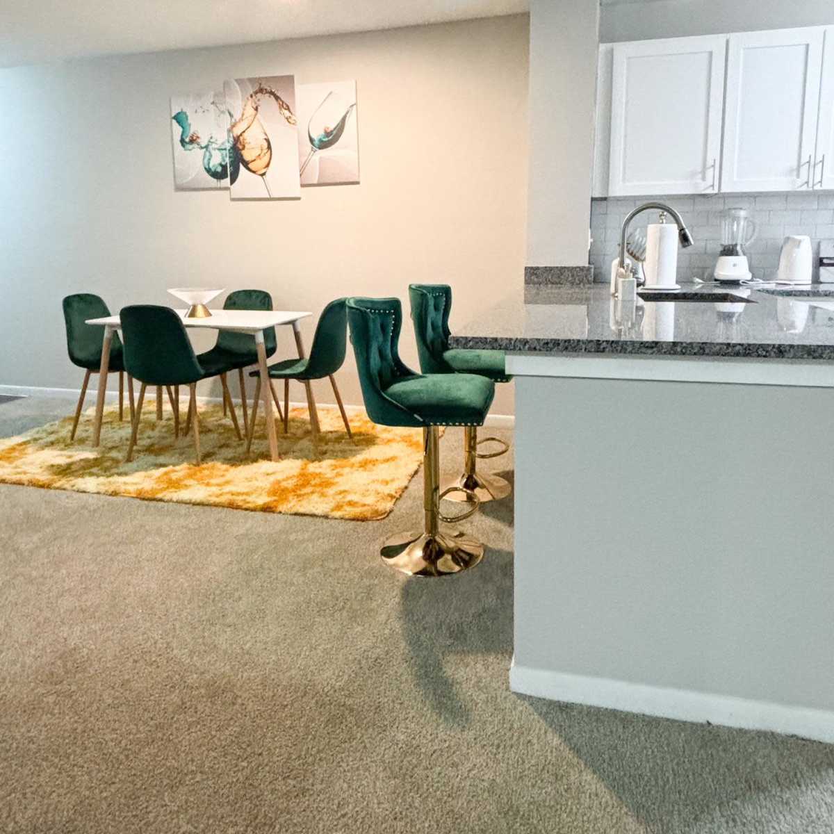 A modern dining area with a white table and green chairs, complemented by a bright yellow rug, all set against a neutral-colored wall.