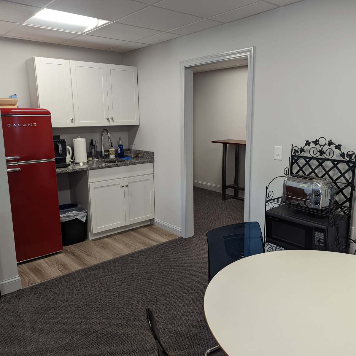 A kitchenette area with a red refrigerator, a countertop with utensils, and a small dining table surrounded by chairs.
