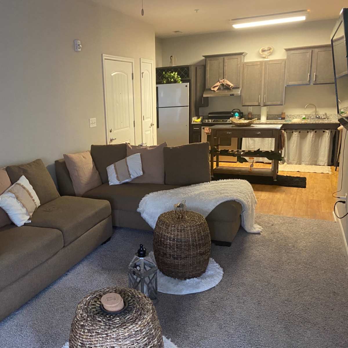 The living room features a sectional sofa, a coffee table, and a view of a kitchen with gray cabinets and a refrigerator.