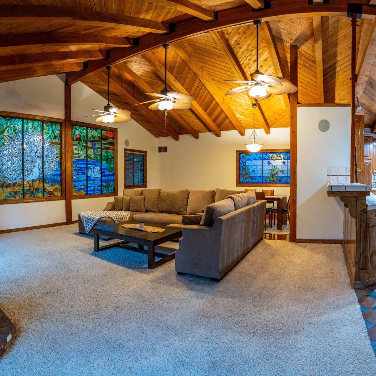 A spacious living area with a high, wooden-beamed ceiling, a sectional sofa, and large stained glass windows, adjacent to a kitchen area.