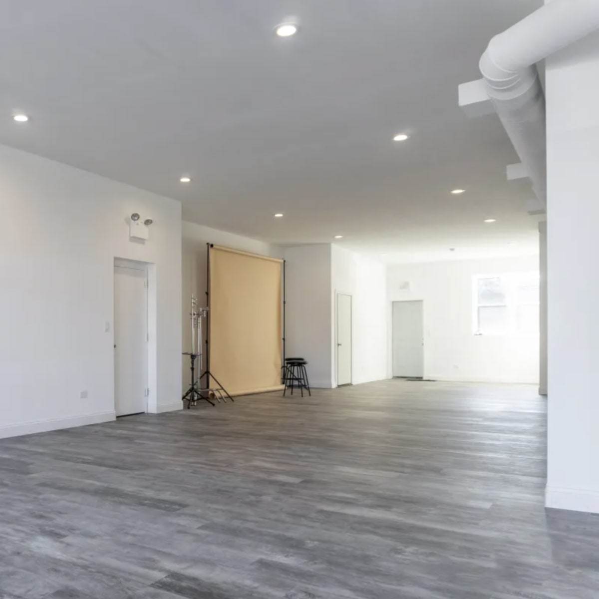 A spacious, empty room with wood-like flooring and bright overhead lights.