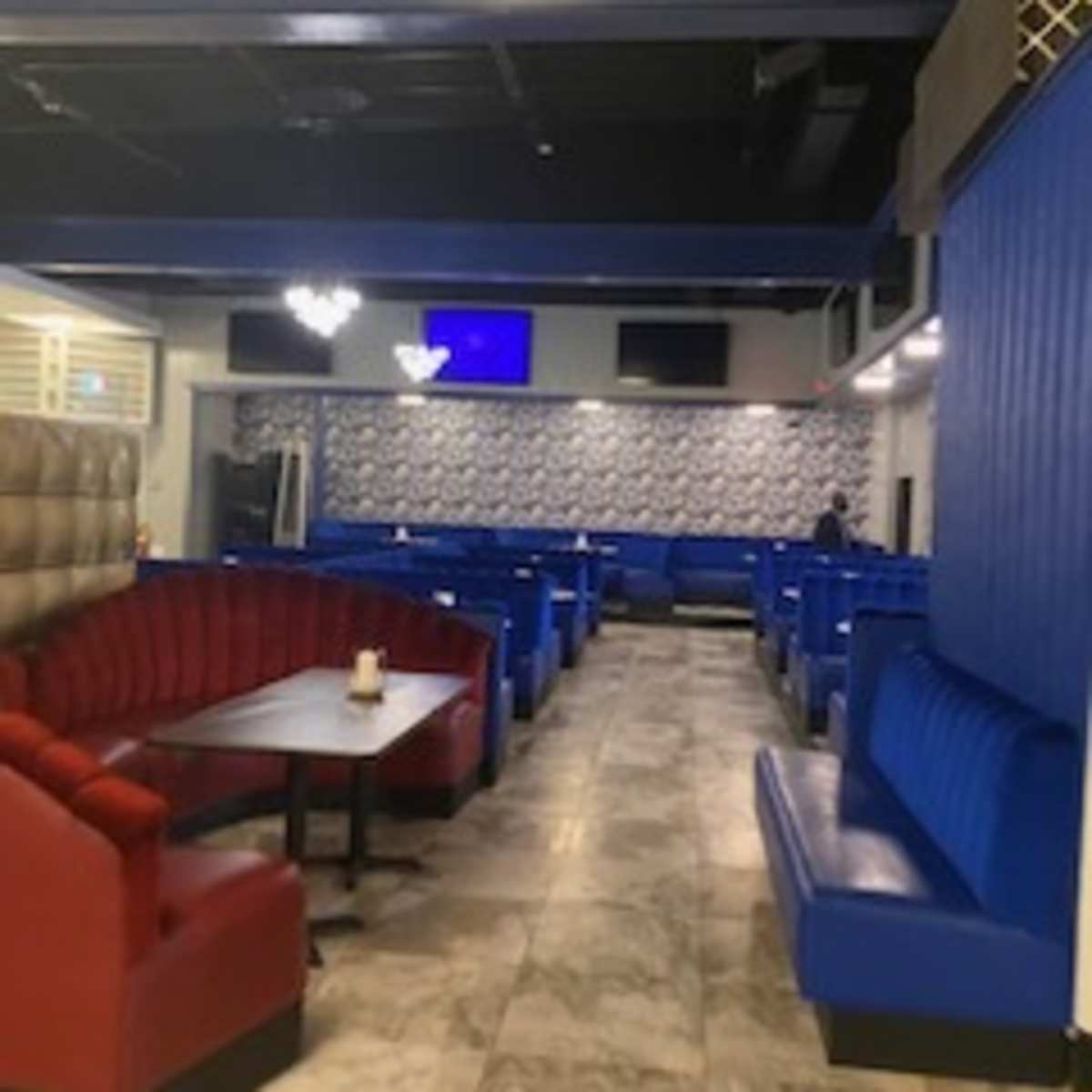 A modern interior of a restaurant with blue and red seating booths arranged around tables on a marble floor.