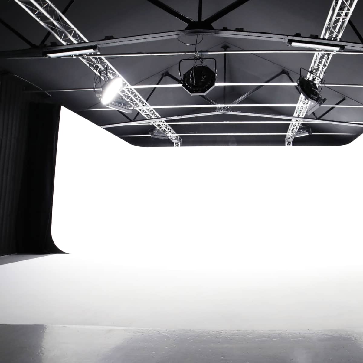 A spacious studio with a white backdrop, suspended lights, and a smooth floor.