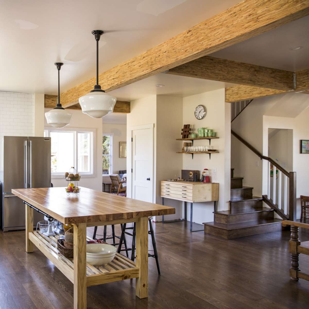 The kitchen features a large center island with a wooden countertop, blue cabinets, stainless steel appliances, and open shelving, alongside a staircase leading to another level.