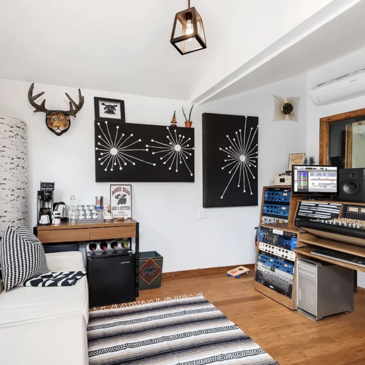 A modern, minimalist studio space featuring a white couch, a wooden desk with a coffee maker, and audio equipment against a backdrop of black and white wall art.