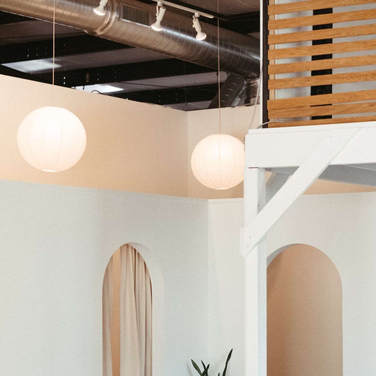 A light-filled interior space with white walls, a potted plant on a small table, and large paper lanterns hanging from the ceiling.