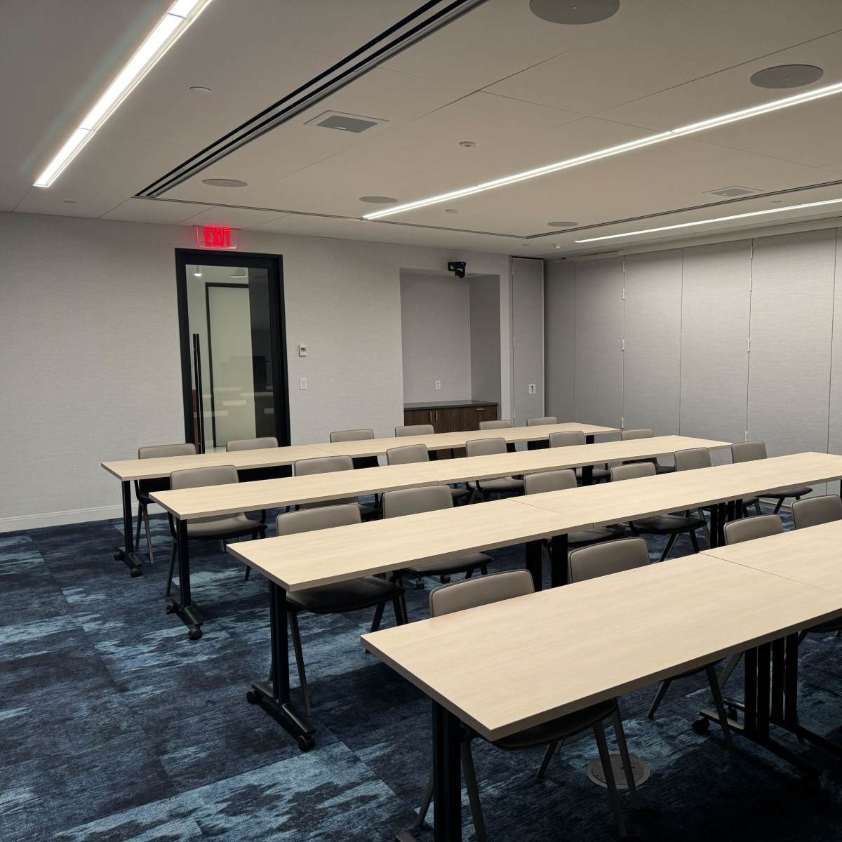 A conference room with rows of wooden tables and chairs arranged in a rectangular layout.