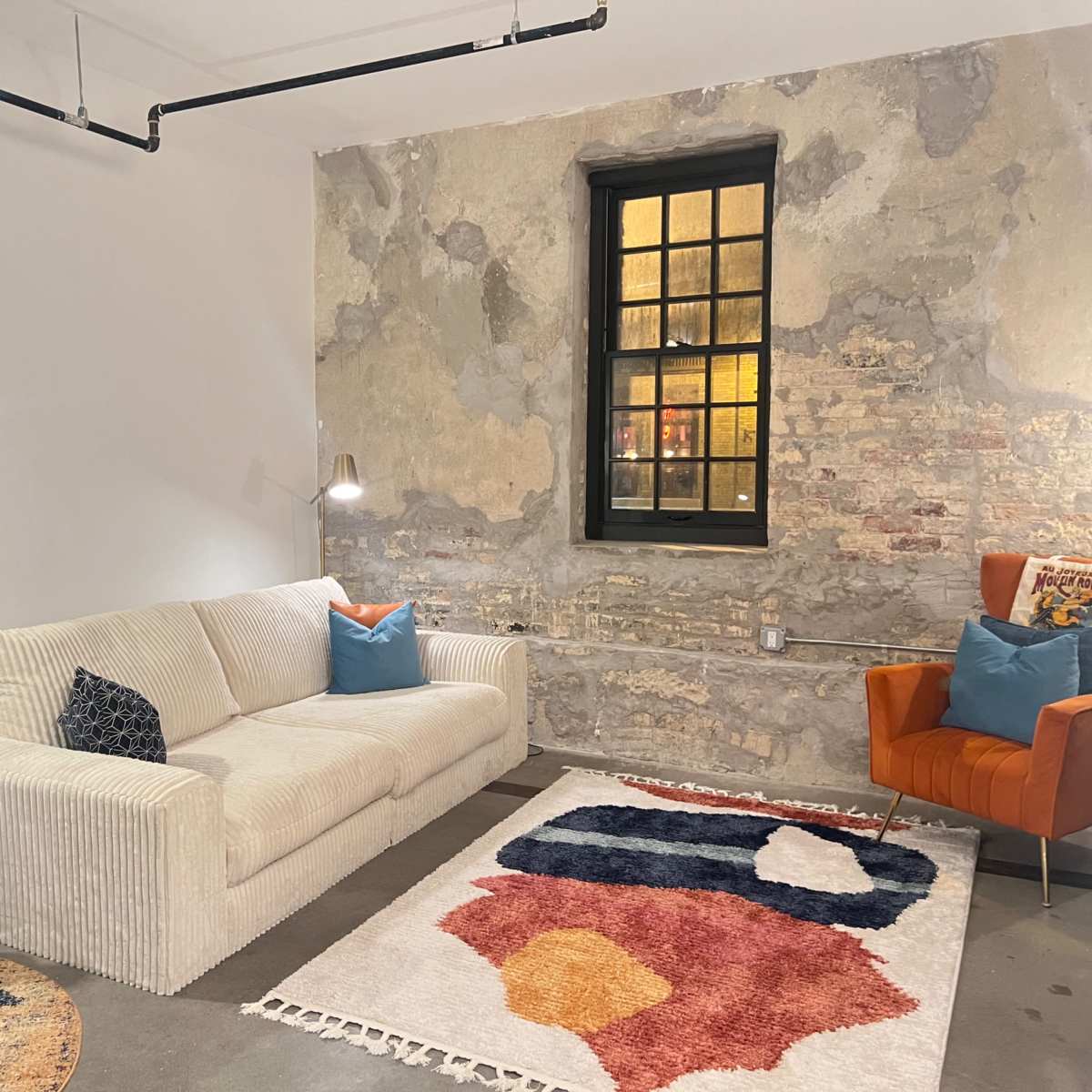 A living room features a white sofa, an orange armchair, a decorative rug, and exposed brick walls.