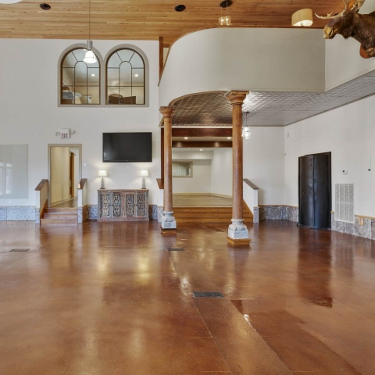 An empty interior space featuring a polished floor, wooden ceilings, decorative pillars, and large windows.