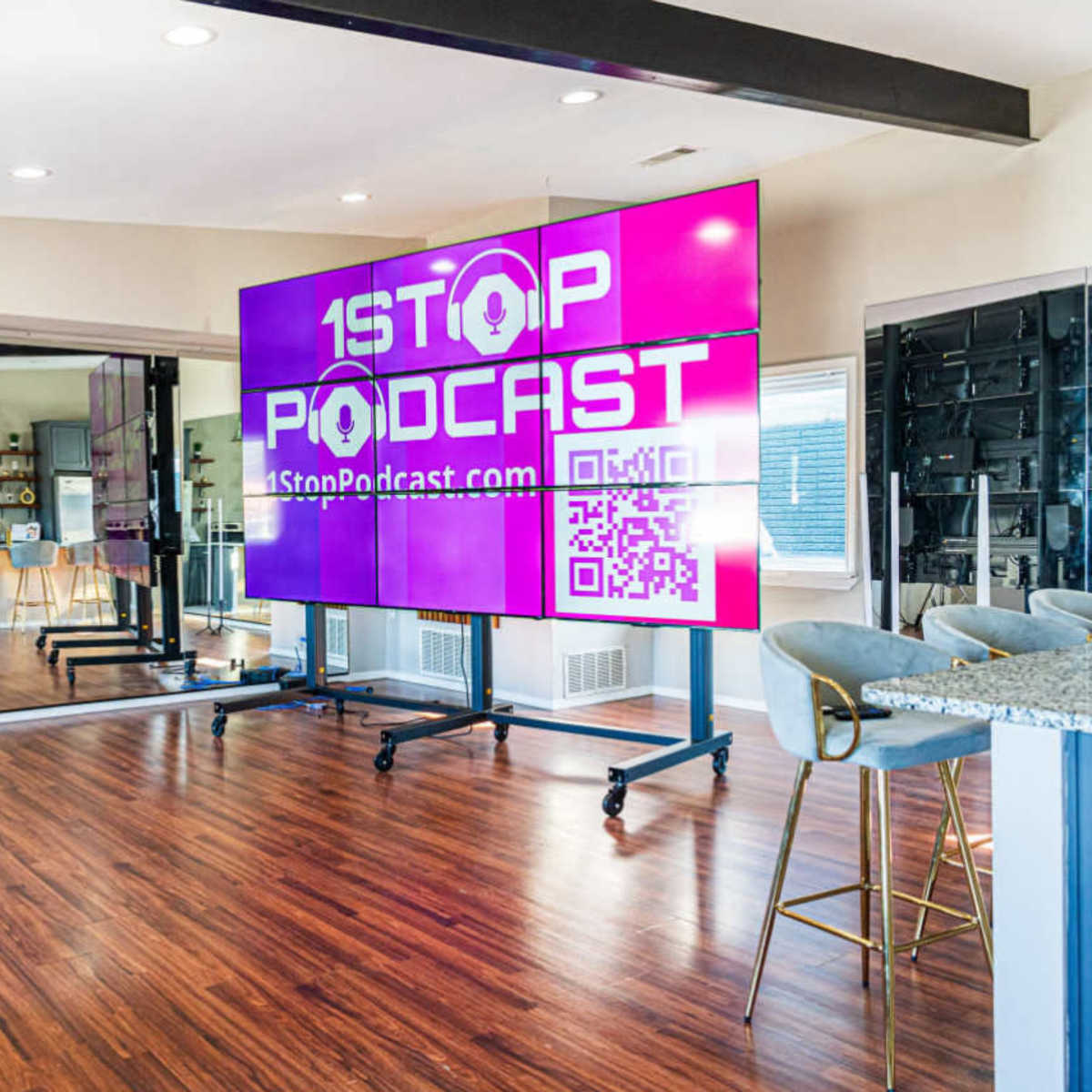 A modern podcast studio with large screens displaying "1Stop Podcast" and a QR code, alongside a kitchen and seating area.
