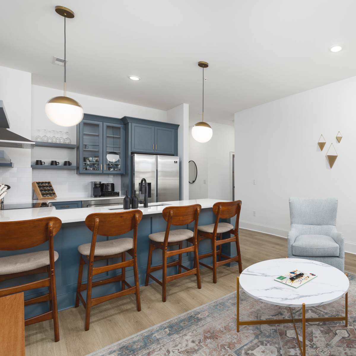 A modern living space featuring a kitchen island with barstools, a beige sofa, a marble coffee table, and a visible bedroom through an open door.
