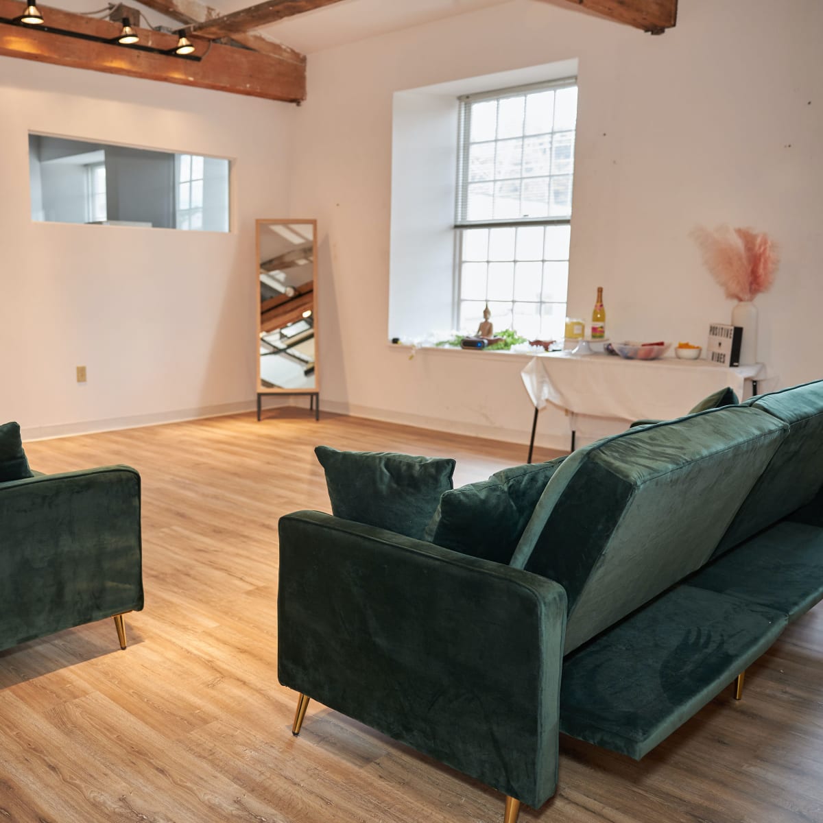 A spacious, well-lit room with two green sofas facing each other and a table adorned with decorative items in the background.