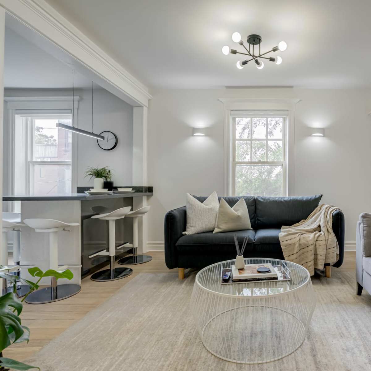 A modern living room with a black sofa, a gray sofa, a round glass coffee table, and a dining area in the background.
