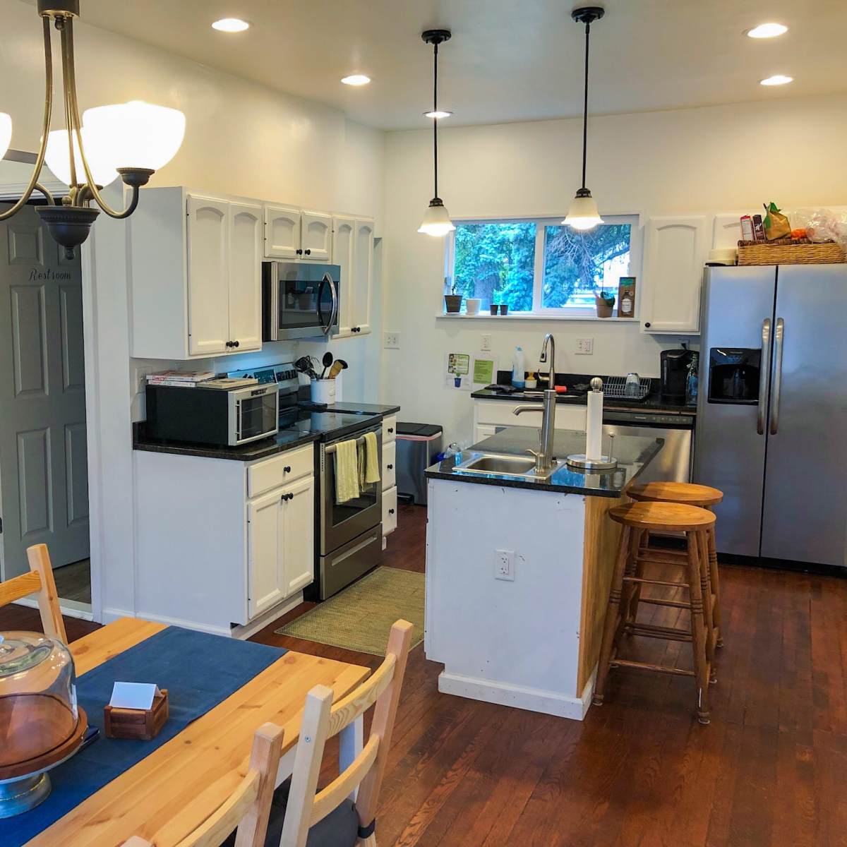 A modern kitchen with white cabinets, stainless steel appliances, and a wooden dining table with a blue table runner.