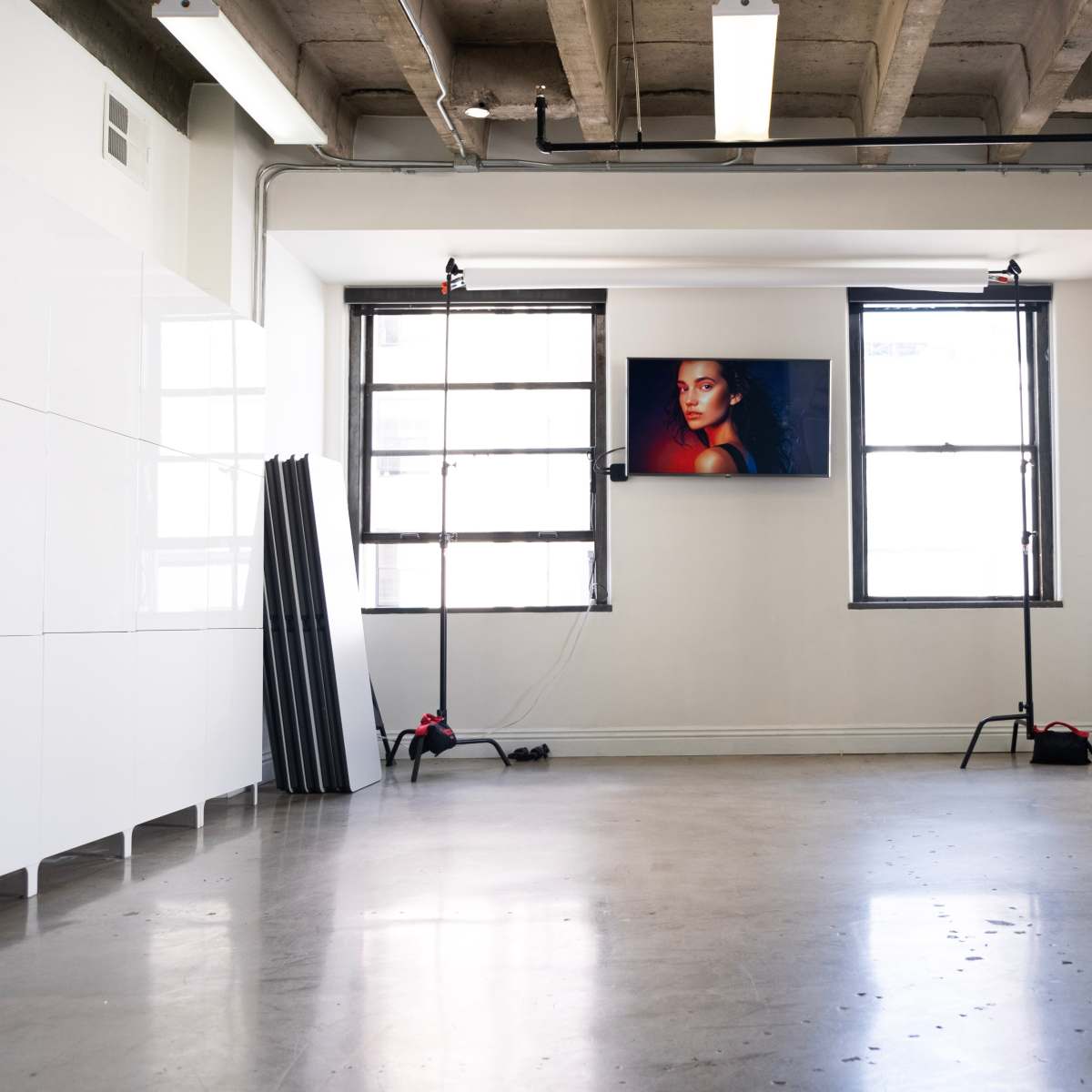 A spacious, modern room features large windows, a flat-screen TV on the wall displaying a portrait, and a minimalistic seating area with a blue chair.