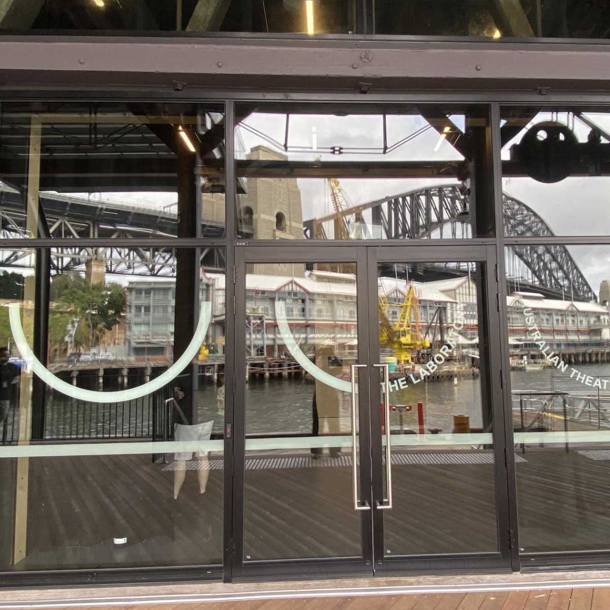 A glass storefront with a view of the Sydney Harbour Bridge and nearby buildings reflected in the windows.