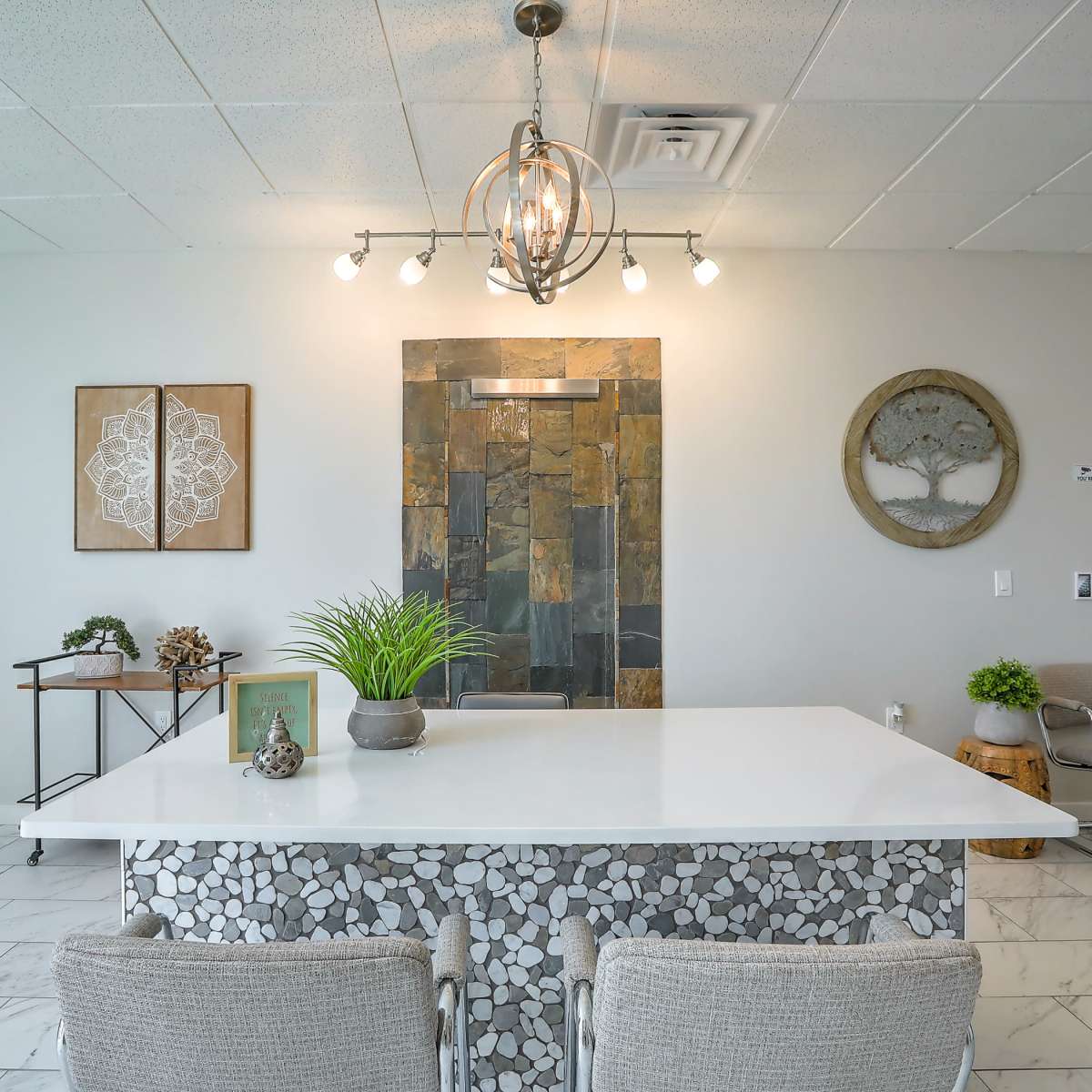 A modern reception area with a large white table, stone wall art, and minimalist decor.