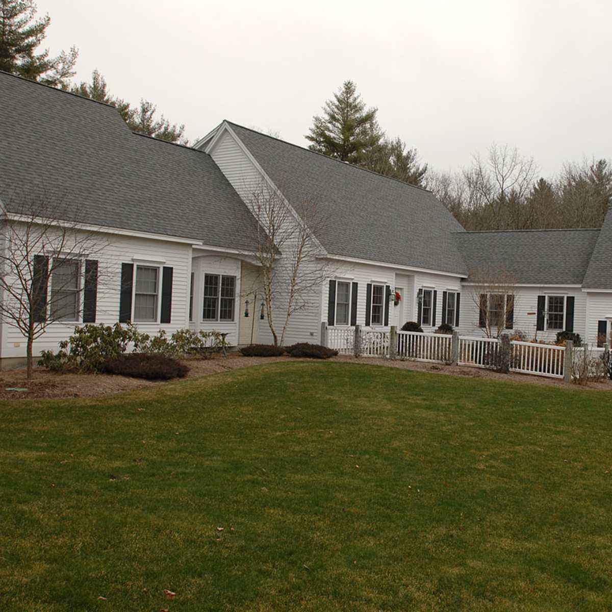 A large white house with multiple sections and a well-maintained lawn, surrounded by trees.