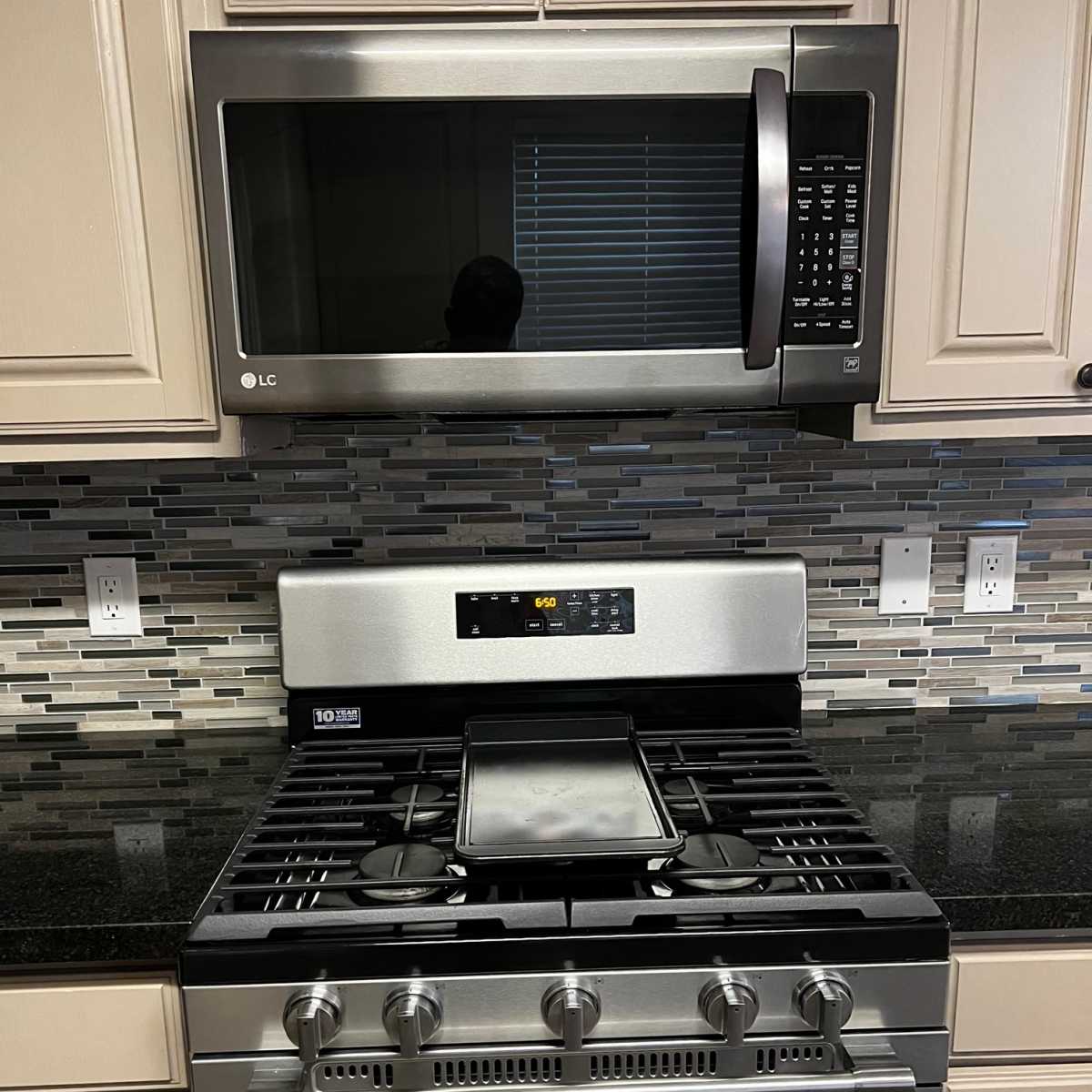 A kitchen setup featuring a stainless steel microwave above a gas range with a black countertop and a tiled backsplash.