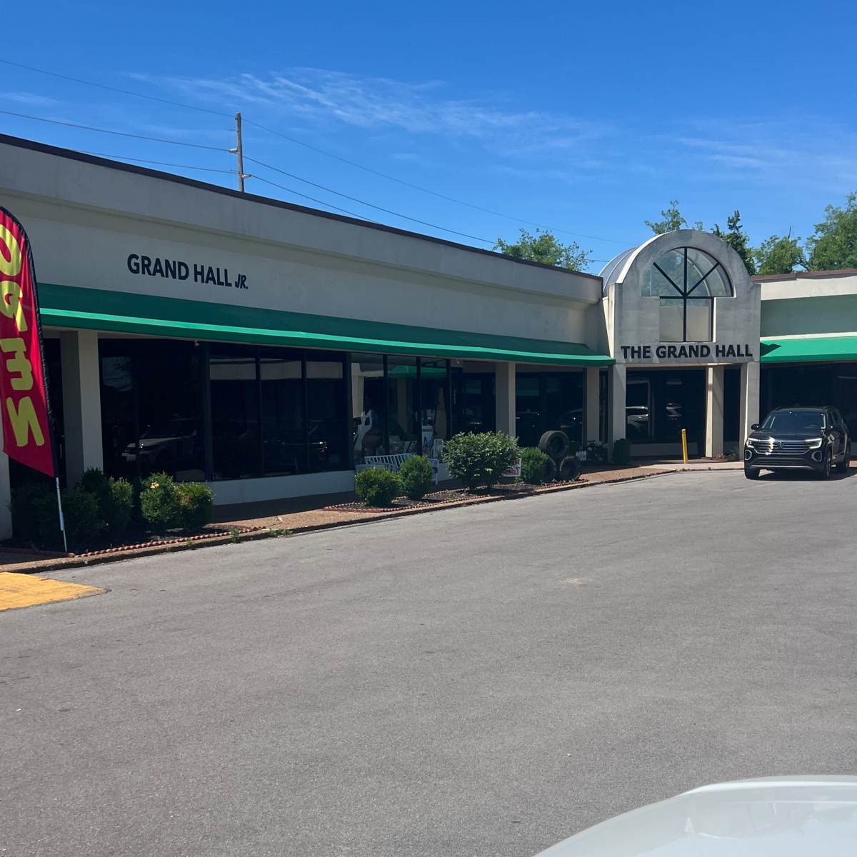 A commercial building labeled "Grand Hall" and "Grand Hall Jr." with a parking area in front and clear blue skies above.
