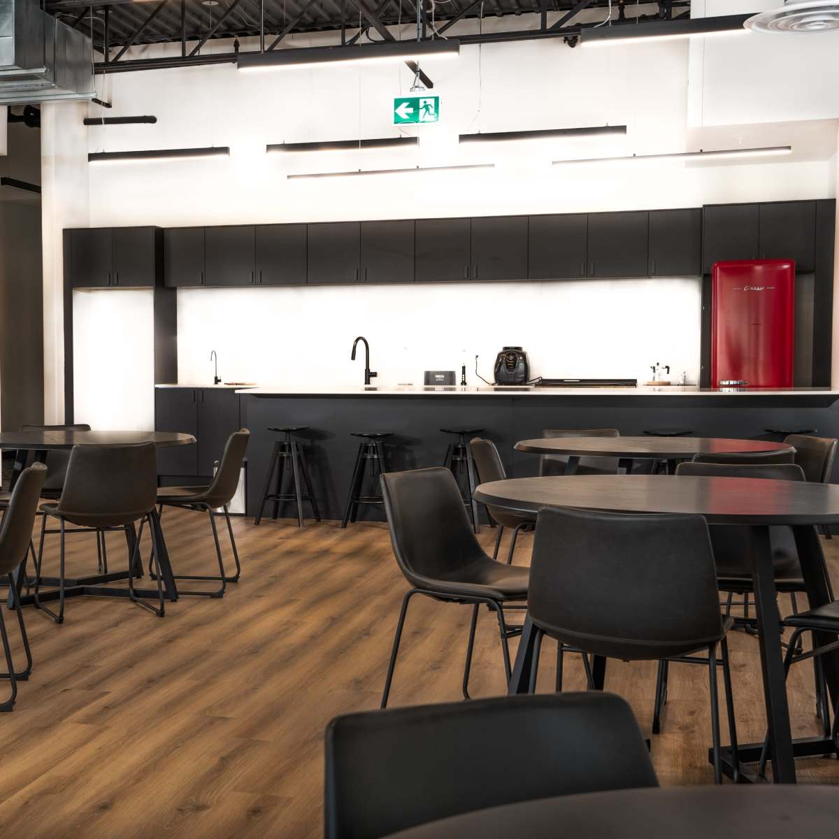 A modern kitchen and dining area with black tables and chairs, wooden flooring, and a sleek kitchen with a red refrigerator and appliances.