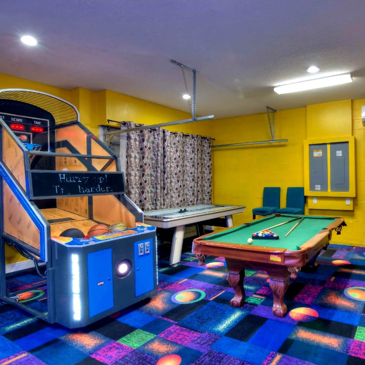 A recreational room featuring an arcade basketball game, a pool table, and colorful carpet tiles.