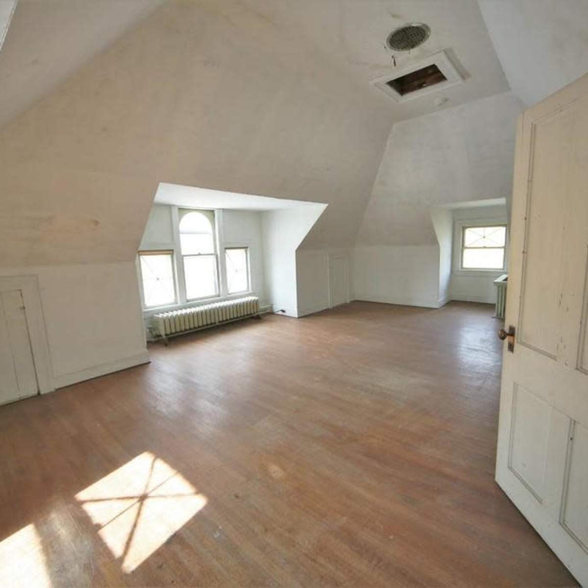 An empty attic room with sloped ceilings, wooden floors, and a few windows allowing natural light to enter.