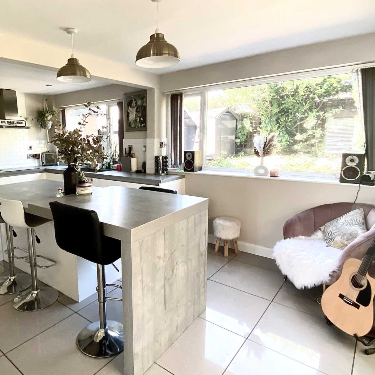 A modern kitchen with a large island, bar stools, and a cozy seating area with a guitar.