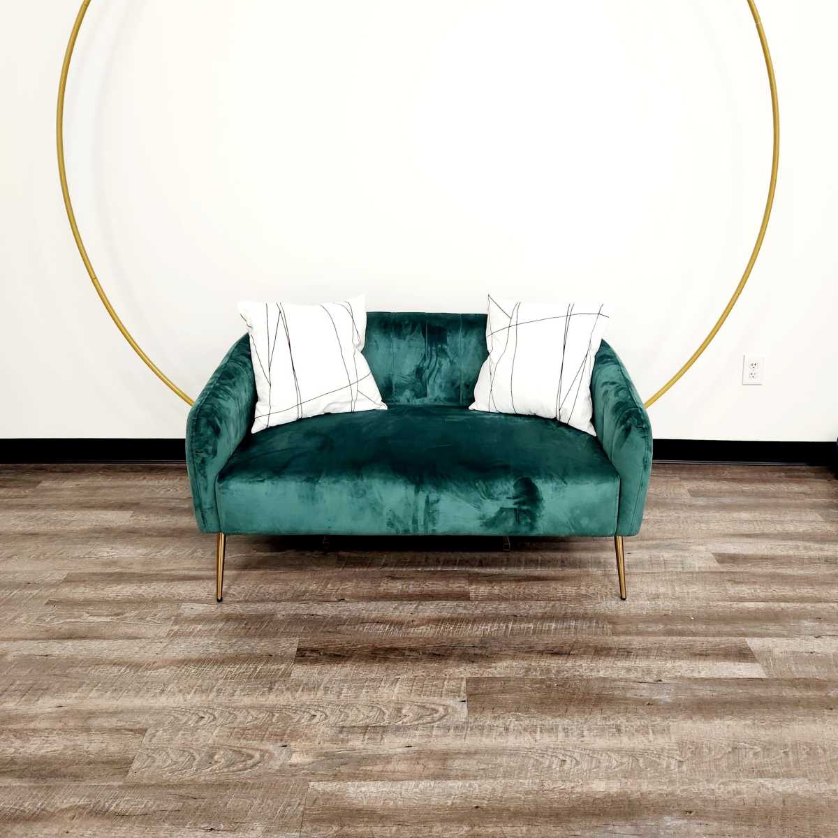 A green velvet couch with gold legs is placed against a wall featuring a large circular gold accent.