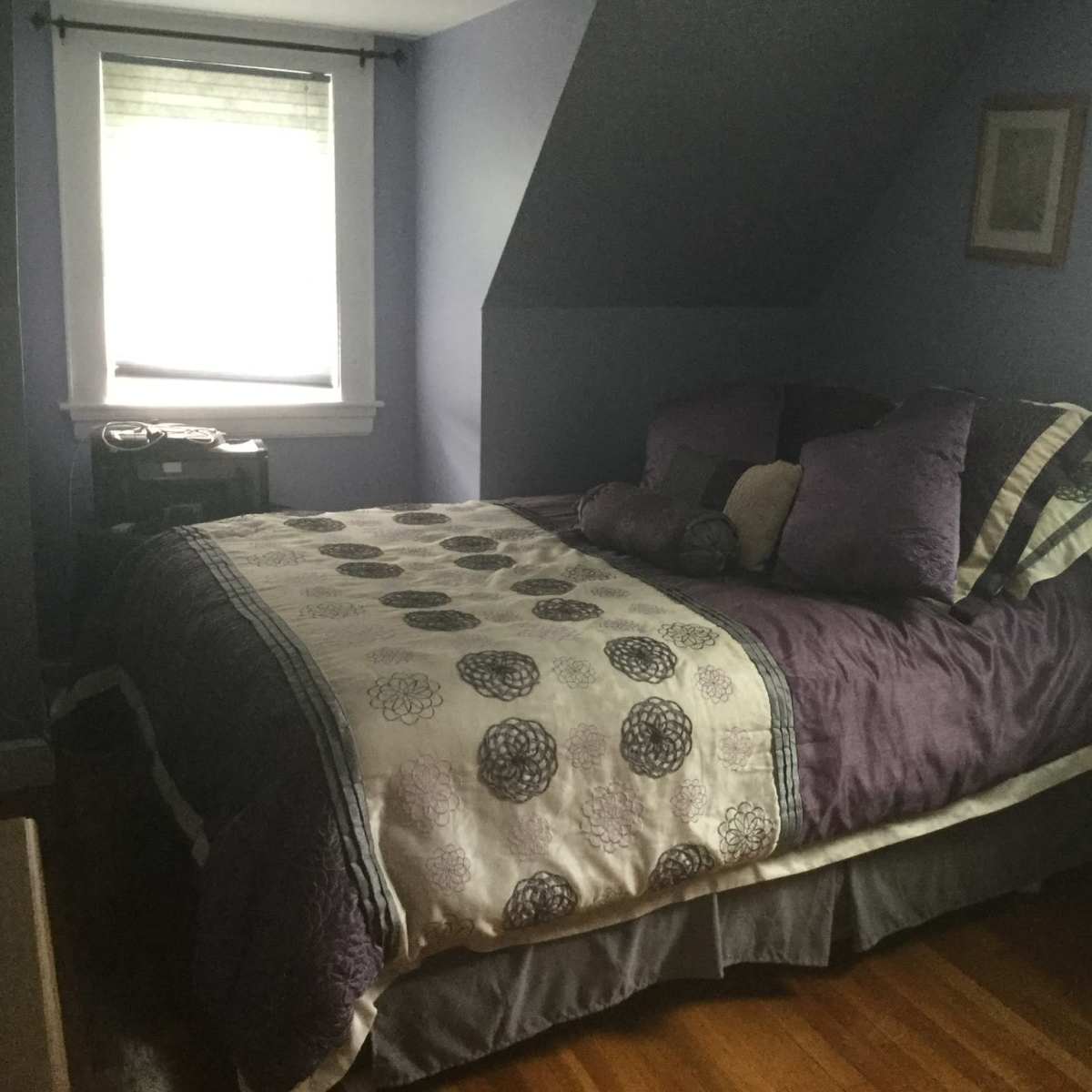 A cozy, slanted-roof bedroom with a bed covered in a decorative quilt and pillows, along with a window letting in natural light.