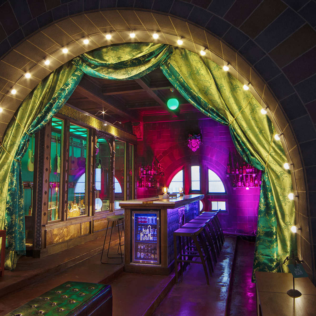 A brightly lit bar area with a decorative archway draped in green curtains and illuminated by string lights.